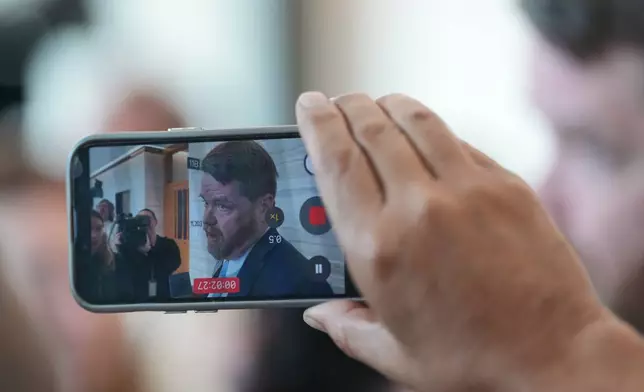 A person records with a smartphone Mark Bankston, an attorney for relatives of the victims of the 2012 Sandy Hook School shooting, as he speaks to the media following a hearing at the county courthouse in Austin, Texas, Thursday, April 30, 2026. (AP Photo/Eric Gay)