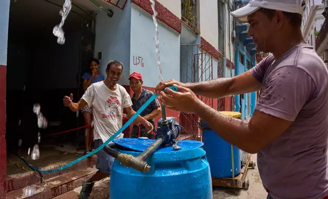 People react as a neighbor places a motor in a container of water by the entrance of their building in Havana, Wednesday, May 27, 2026. (AP Photo/Ramon Espinosa)