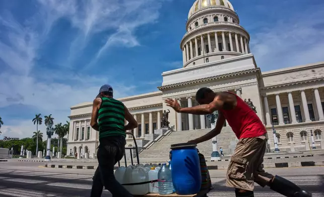 People carry containers of water past the Capitol in Havana, Wednesday, May 27, 2026. (AP Photo/Ramon Espinosa)