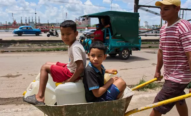 A man transports containers of water with his children in Havana, Thursday, May 28, 2026. (AP Photo/Ramon Espinosa)