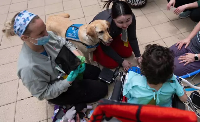 Cincinnati Children's Hospital facility dog Hadley and hospital staff including registered nurse Hanna Hill, right, look to 5-year-old patient Calvin Owens during a physical therapy visit on the patio of Cincinnati Children's Hospital in Cincinnati, Monday, May 4, 2026. (AP Photo/Carolyn Kaster)