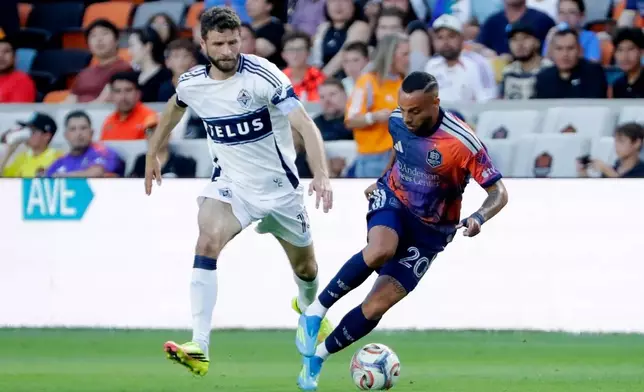 Houston Dynamo FC midfielder Guilherme Santos, right, moves the ball past Vancouver Whitecaps FC midfielder Thomas Muller during the first half of an MLS soccer match, Saturday, May 16, 2026, in Houston. (AP Photo/Michael Wyke)