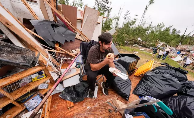 Logan Branch eats a hotdog as he sits among the debris of what is left of his home at Gene's Mobile Home Supply, a trailer park in Bogue Chitto, Miss., Thursday, May, 7, 2026, after a tornado cut across the state. (AP Photo/Gerald Herbert)