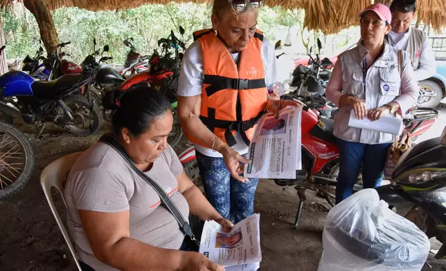 Julia Margarita Bravo Diaz, of Cuba, wearing life jacket, shows photos of missing people, including her daughter Meiling Álvarez Bravo and grandson Samei Armando Reyes Álvarez, to local residents in San Jose Hueyate, Chiapas state, Mexico, Saturday, May 9, 2026, during a search for migrants who vanished in late 2024 along a maritime smuggling route to the U.S. (AP Photo/Edgar H. Clemente)
