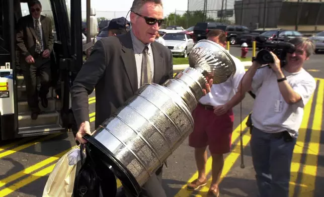 FILE - New Jersey Devils head coach Larry Robinson carries the Stanley Cup from the bus as the team arrives back in East Rutherford, N.J., June 11, 2000. (AP Photo/Daniel Hulshizer)
