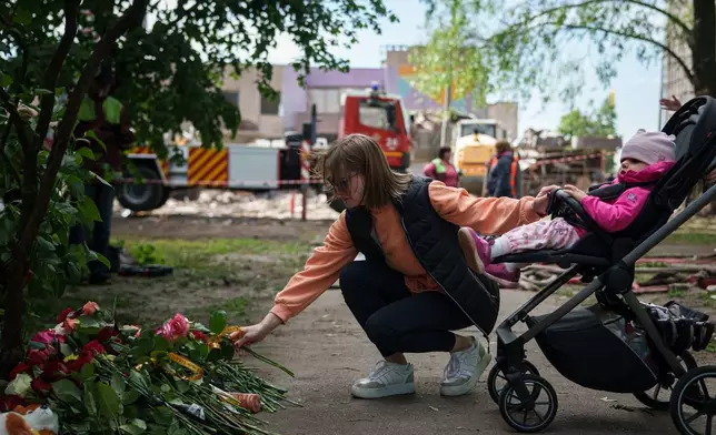 A woman lays flowers in front of a house heavily damaged after a Russian strike on residential neighbourhood in Kyiv, Ukraine, on Friday, May 15, 2026. (AP Photo/Evgeniy Maloletka)