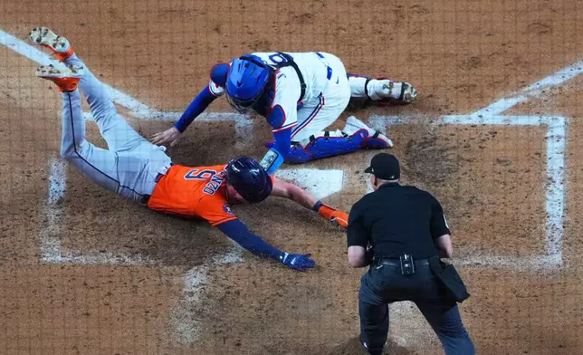 Houston Astros' Zach Dezenzo, left, slides in to score ahead of the tag by Texas Rangers catcher Danny Jansen, top, on a bunt by Astros' Christian Vázquez, not visible, as home plate umpire Paul Clemons looks on during the fifth inning of a baseball game Monday, May 25, 2026, in Arlington, Texas. (AP Photo/Julio Cortez)