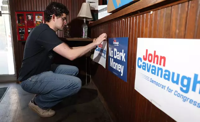 Gabe Kaplan, deputy finance director for State Sen. John Cavanaugh's campaign, posts signs in Underwood Bar ahead the election night watch party for the Democratic nomination to the House of Representatives in Nebraska's second district, Tuesday, May 12, 2026, in Omaha, Neb. (AP Photo/Rebecca S. Gratz)