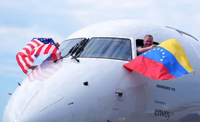 Capt. Ric Wilson waves a Venezuelan flag and the first officer waves a U.S. flag as they prepare to fly American Airlines Flight AA3599, the first direct commercial flight between the United States and Venezuela in seven years, Thursday, April 30, 2026, at Miami International Airport in Miami. (AP Photo/Rebecca Blackwell)
