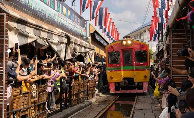 A crowd of tourists take pictures of a passing train at the Mae Klong Railway Market near Bangkok, Thailand on Dec. 6, 2025. (AP Photo/Anton L. Delgado)