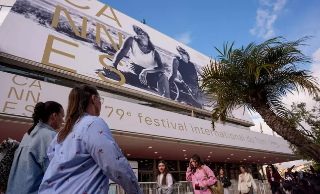 People walk past the Palais des Festivals during preparations for the 79th international film festival, Cannes, southern France, Monday, May 11, 2026. (AP Photo/Andreea Alexandru)