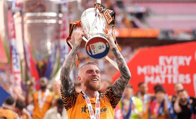 Hull City's Oliver McBurnie celebrates with the trophy after winning promotion to the Premier League following the Championship play-off final between Hull City and Middlesbrough at Wembley Stadium, London, Saturday May 23, 2026. (Adam Davy/PA via AP)