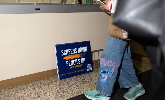Signs reading, "Screens down, pencils up," are seen a school board meeting at the Lower Merion School District Administration Building on Monday, May 11, 2026, in Ardmore, Pa. (AP Photo/Joe Lamberti)