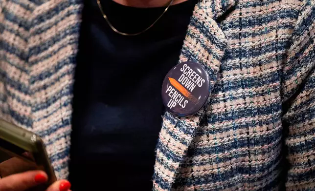 An attendee wears a, "Screens down, pencils up," button during a school board meeting at the Lower Merion School District Administration Building on Monday, May 11, 2026, in Ardmore, Pa. (AP Photo/Joe Lamberti)