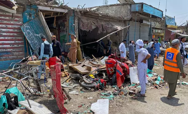 Plainclothes police officers, left, and local residents examine damage at the site of a bomb explosion at a market in Sarai Norag in Lakki Marwat, a district in Pakistan's Khyber Pakhtunkhwa province, Tuesday, May 12, 2026. (AP Photo/Farhat Ullah)