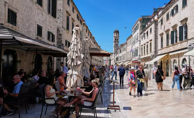 People sit in a cafe as others walk on the main street of Stradun in old town Dubrovnik, Croatia, Monday, April 27, 2026. (AP Photo/Darko Bandic)