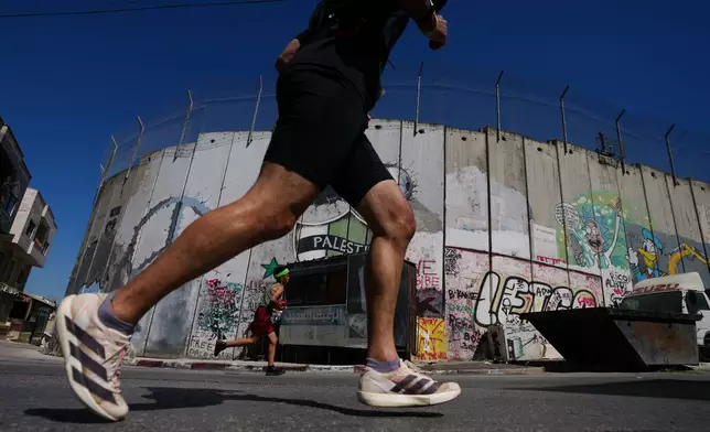 Runners pass by Israel's separation wall as they compete in the Palestine Marathon in the West Bank city of Bethlehem, Friday, May 8, 2026. (AP Photo/Mahmoud Illean)