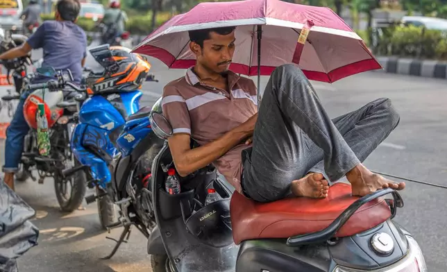A motorcyclist rests under an umbrella while waiting in line for fuel at a petrol station in Dhaka, Bangladesh, Thursday, April 23, 2026. (AP Photo/Abdul Goni)