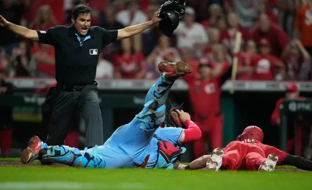 Home plate umpire John Tumpane calls Cincinnati Reds' Spencer Steer, right, safe as he dives into home plate to score the game winning run on a single hit by Blake Dunn as St. Louis Cardinals catcher Yohel Pozo, center, follows with the late tag in the eleventh inning of the second baseball game of a doubleheader in Cincinnati, Saturday, May 23, 2026. (AP Photo/Carolyn Kaster)