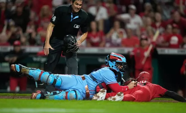 Home plate umpire John Tumpane looks on as Cincinnati Reds' Spencer Steer, right, is safe as he dives into home plate to score the game winning run on a single hit by Blake Dunn as St. Louis Cardinals catcher Yohel Pozo, center, follows with the late tag in the eleventh inning of the second baseball game of a doubleheader in Cincinnati, Saturday, May 23, 2026. (AP Photo/Carolyn Kaster)