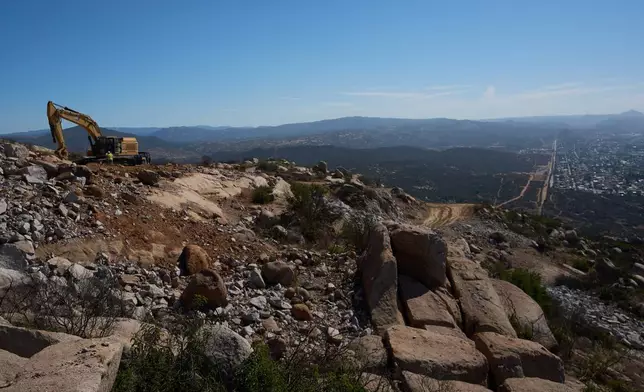 Construction crews work on a new border wall segment on Kuuchamaa Mountain, Friday, April 24, 2026, seen from Tecate, Mexico. (AP Photo/Gregory Bull)