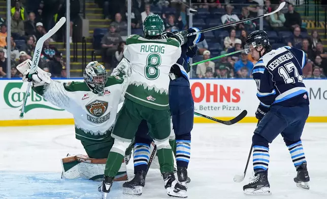 The puck deflects off of Chicoutimi Sagueneens' Christophe Berthelot, back centre, as he's checked by Everett Silvertips' Kayd Ruedig (8) in front of goalie Anders Miller (31) as Chicoutimi's Thomas Desruisseaux (17) watches during the second period of a Memorial Cup hockey game in Kelowna, British Columbia, Saturday, May 23, 2026. (Darryl Dyck/The Canadian Press via AP)