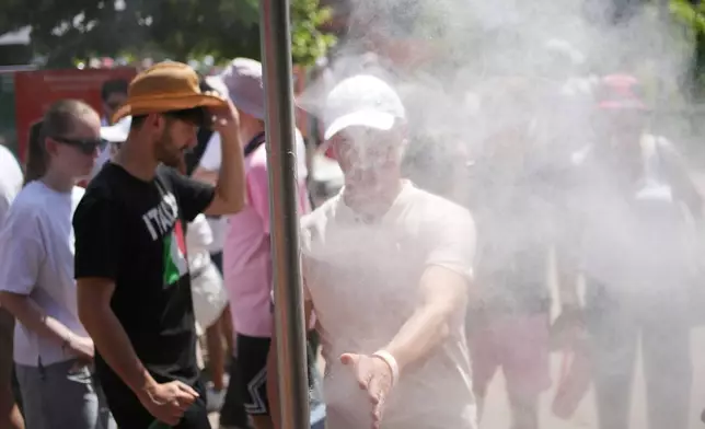 Visitors cool themselves with water from sprinklers during a hot day at the French Open tennis tournament in Paris, Monday, May 25, 2026. (AP Photo/Christophe Ena)
