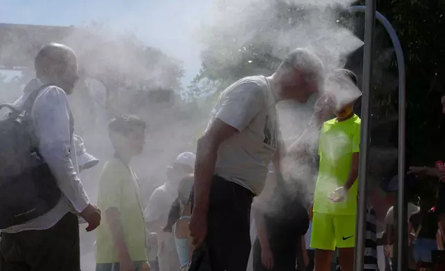 Visitors cool themselves with water from sprinklers during a hot day at the French Open tennis tournament in Paris, Monday, May 25, 2026. (AP Photo/Aurelien Morissard)