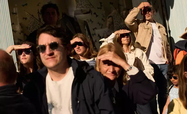 People shield their eyes from the sun while watching the red carpet during the 79th international film festival, Cannes, southern France, Friday, May 15, 2026. (AP Photo/John Locher)