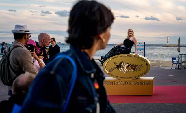 A woman poses for people on top of a sign of Festival de Cannes during the 79th international film festival, Cannes, southern France, Thursday, May 14, 2026. (AP Photo/Andreea Alexandru)