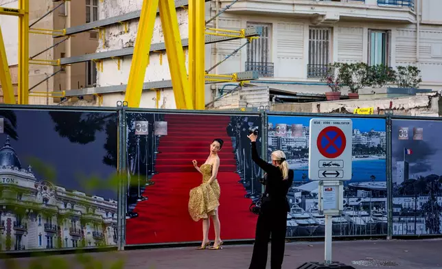 A woman poses for a photographer in front of a poster showcasing the famous red carpet during the 79th international film festival, Cannes, southern France, Thursday, May 14, 2026. (AP Photo/Andreea Alexandru)