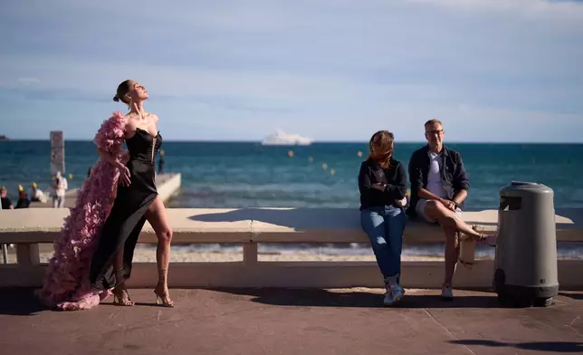 A festivalgoer poses for photographers as people sit by the beach along the Croisette during the 79th international film festival, Cannes, southern France, Friday, May 15, 2026. (AP Photo/John Locher)