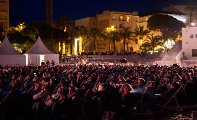 A woman checks her phone as people wait for the start of a movie on the beach during the 79th international film festival, Cannes, southern France, Friday, May 15, 2026. (AP Photo/Andreea Alexandru)