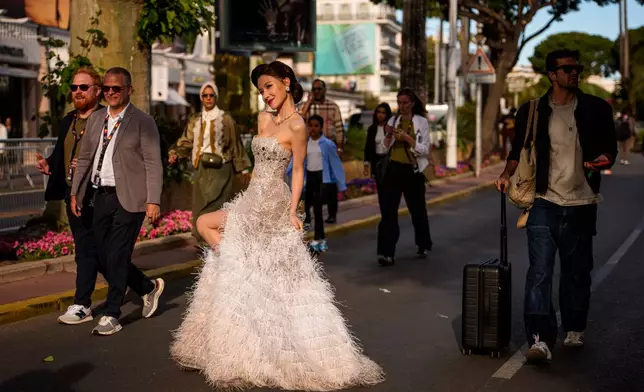 People walk past a woman posing for photographers after walking on the red carpet for the movie "Parallel Talles" during the 79th international film festival, Cannes, southern France, Thursday, May 14, 2026. (AP Photo/Andreea Alexandru)