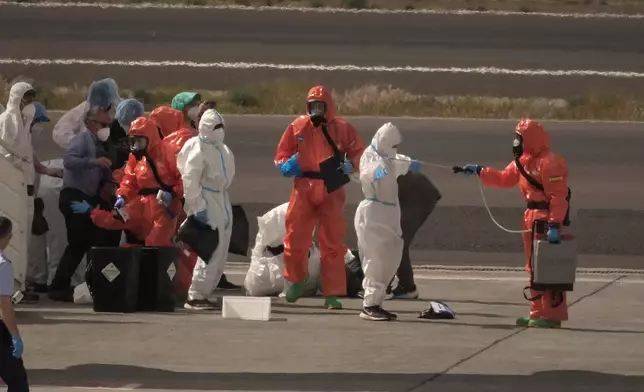 Passengers are sprayed with disinfectant by Spanish government officials before boarding a plane after disembarking from the hantavirus-stricken cruise ship MV Hondius at Tenerife airport in the Canary Islands, Spain, Sunday, May 10, 2026. (AP Photo/Arturo Rodriguez)