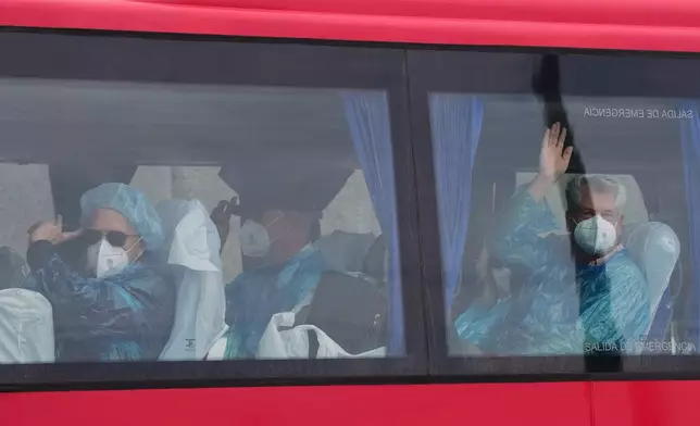 Passengers wave inside a bus after being disembarked from the hantavirus-stricken cruise ship MV Hondius at the port of Granadilla in Tenerife, Canary Islands, Spain, Sunday, May 10, 2026. (AP Photo/Manu Fernandez)