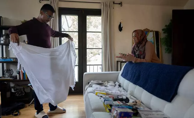 Faisal Rashid, left, practices putting on his ihram robe as he speaks with his wife Samiha Matin as they packfor the annual Hajj pilgrimage in Mecca, Saudi Arabia, at their home in Pasadena, Calif, Sunday, May 17, 2026. (AP Photo/Ryan Sun)