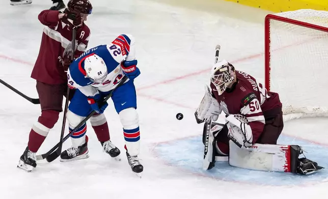 From left, Latvia's Kristaps Zile, USA's Mathieu Olivier and Latvia's goaltender Kristers Gudlevskis challenge for the puck during the 2026 IIHF Men's Ice Hockey World Championship preliminary round group A match between Latvia and the United States in Zurich, Switzerland, Saturday, May 23, 2026. (Andreas Becker/Keystone via AP)
