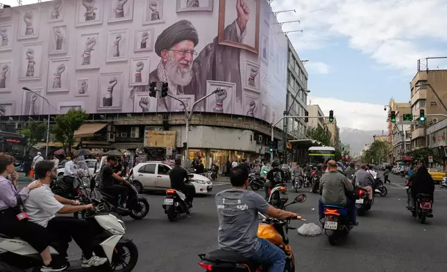 Motorbikes drive past a billboard with graphic showing the late Iranian Supreme Leader Ayatollah Ali Khamenei, who was killed in the U.S. and Israel strikes on Feb. 28, with his framed fist amongst his supporters framed fists in downtown Tehran, Iran, Wednesday, May 6, 2026. (AP Photo/Vahid Salemi)