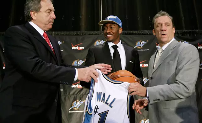 FILE - Washington Wizards first draft pick John Wall, center, from the University of Kentucky, smiles as he holds up a ball and jersey with coach Flip Saunders, right, and Wizards president Ernie Grunfeld, during a news conference in Washington, June 25, 2010. (AP Photo/Alex Brandon, File)