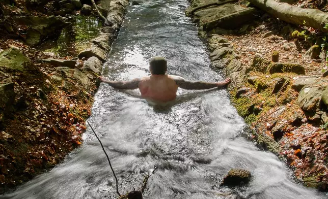 A man takes a bath in the ice cold Urselbach creek in a forest of the Taunus region near Frankfurt, Germany, Sunday, April 26, 2026. (AP Photo/Michael Probst)