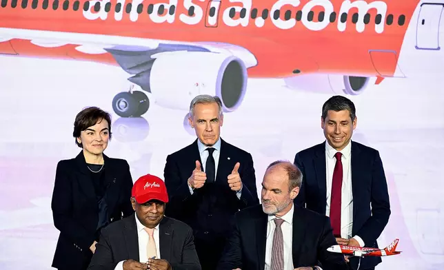 Quebec Premier Christine Frechette, back left, Canada's Prime Minister Mark Carney, centre, and Guillaume Chevasson, CEO, Airbus Canada, back right, look on as Lars Wagner, CEO, Airbus Commercial Aircraft, front right, and AirAsia CEO Tony Fernandes, front left, sign a landmark order for 150 Airbus A220 aircraft during an event at the Airbus A220 Delivery Center in Mirabel, Que., Wednesday, May 6, 2026. (Graham Hughes/The Canadian Press via AP)