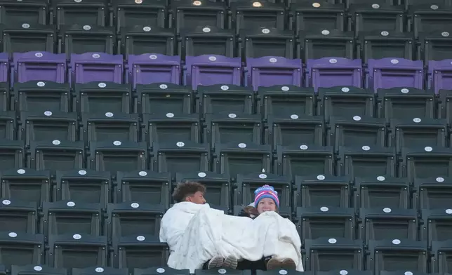 Fans use a blanket to keep warm as temperatures drop to near freezing as the Colorado Rockies host the New York Mets in the second inning of a baseball game, Wednesday, May 6, 2026, in Denver. (AP Photo/David Zalubowski)