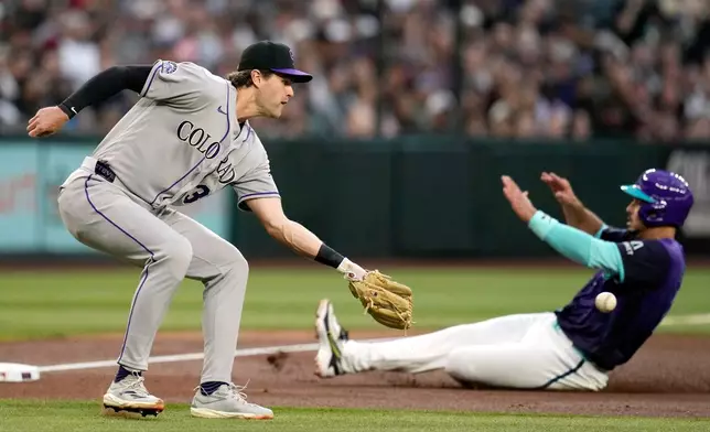 Colorado Rockies third baseman Chad Stevens, left, reaches out to catch a late throw as Arizona Diamondbacks' Nolan Arenado advances to third base during the second inning of a baseball game, Friday, May 22, 2026, in Phoenix. (AP Photo/Ross D. Franklin)