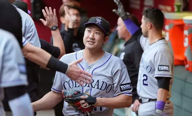 Colorado Rockies starting pitcher Tomoyuki Sugano, of Japan, smiles as he his greeted in the team dugout after warming up prior to a baseball game against the Arizona Diamondbacks, Friday, May 22, 2026, in Phoenix. (AP Photo/Ross D. Franklin)