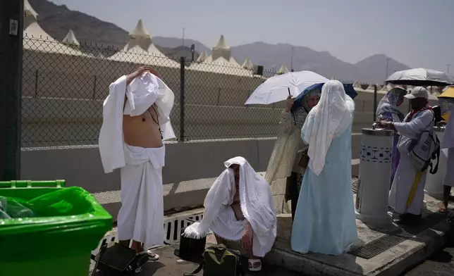 Muslim pilgrims cover their heads to avoid sunlight as they rest while on their way to cast pebbles at pillars in the symbolic stoning of the devil, the last rite of the annual Hajj, in Mina near the holy city of Mecca, Saudi Arabia, Wednesday, May 27, 2026. (AP Photo/Altaf Qadri)