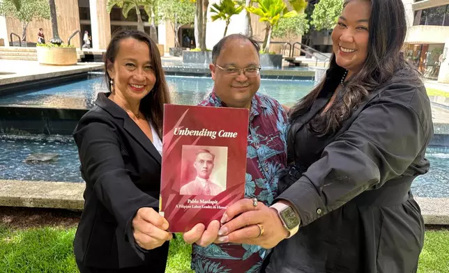 Attorneys Becky Gardner, left, Daniel Padilla, center, and Kainani Collins Alvarez pose with a book about Filipino labor leader Pablo Manlapit on Wednesday, May 27, 2026, in Honolulu. (AP Photo/Jennifer Sinco Kelleher)