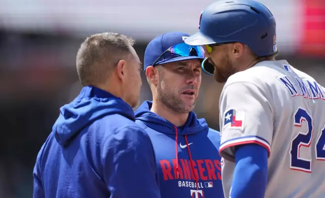 Texas Rangers' Brandon Nimmo, right, confers with manager Skip Schumaker, center, and a trainer before leaving the field after legging out a single in the fifth inning of a baseball game agaisnt the Colorado Rockies, Wednesday, May 20, 2026, in Denver. (AP Photo/David Zalubowski)