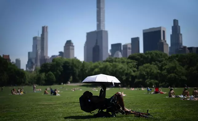 A person uses an umbrella to shield themselves from the sun during a heat advisory in Central Park, Tuesday, May 19, 2026, in New York. (AP Photo/Adam Gray)