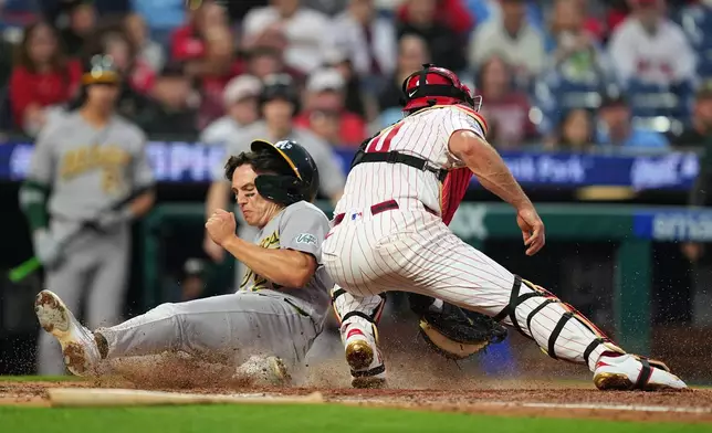 Athletics' Zack Gelof scores past Philadelphia Phillies catcher J.T. Realmuto during the fifth inning of a baseball game, Wednesday, May 6, 2026, in Philadelphia. (AP Photo/Matt Rourke)